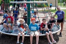 Group of children on a playground with summer counselor smiling for the camera
